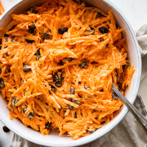 A carrot raisin salad in a white bowl with a spoon.