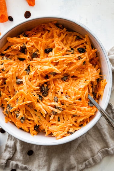 A carrot raisin salad in a white bowl with a spoon.