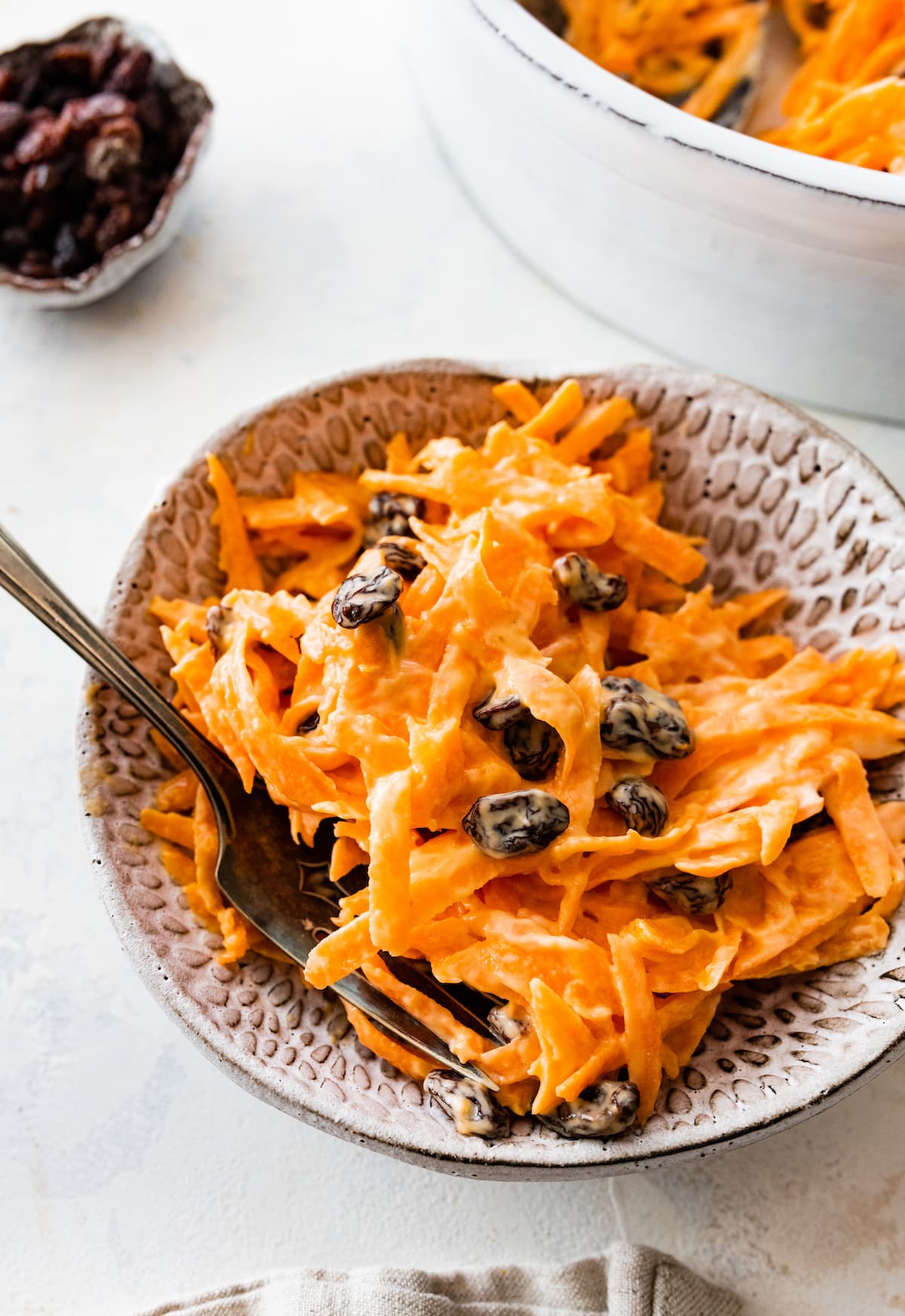 A carrot raisin salad in a small bowl with a fork.