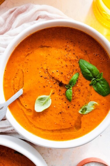 Tomato basil soup garnished with a drizzle of oil and fresh basil in a bowl.