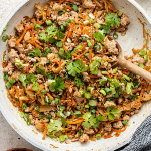 A skillet containing egg roll in a bowl. A wooden serving spoon rests in the pan.