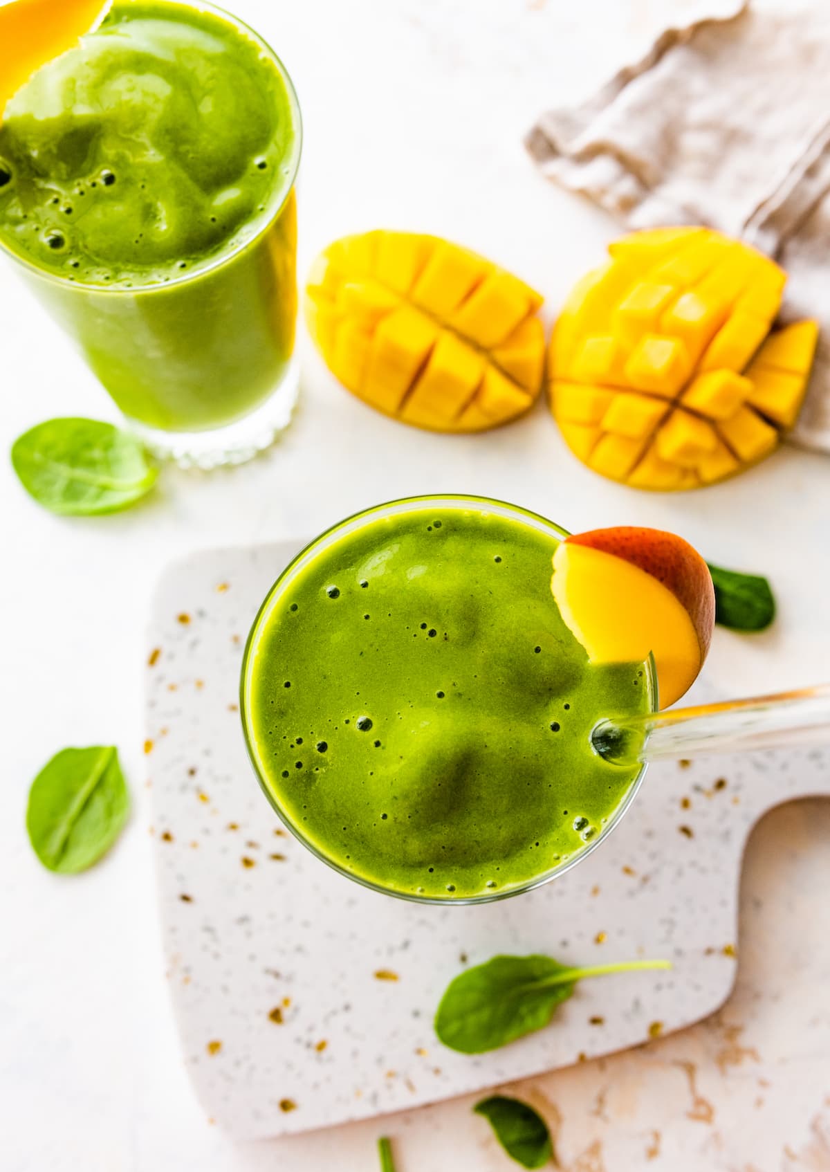 Overhead of two green smoothies in glasses with fresh mango slices.