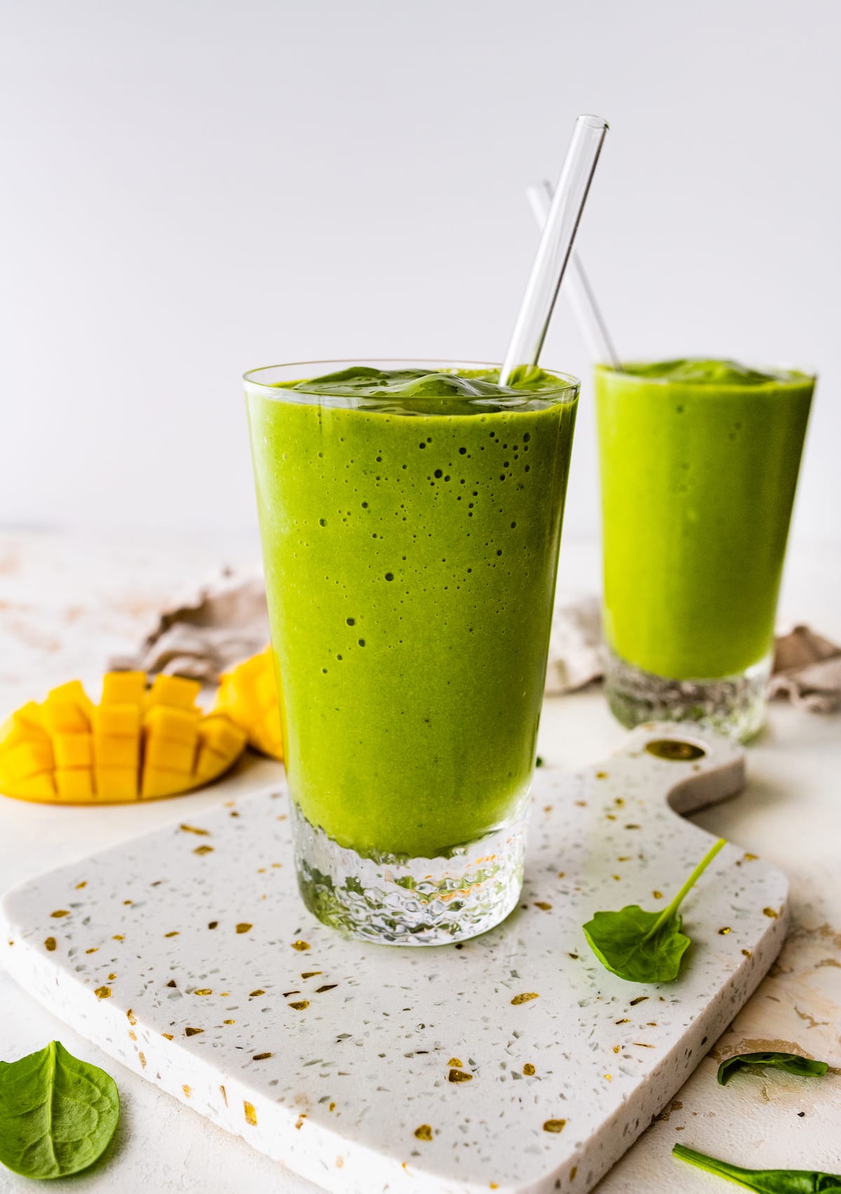Two green smoothies in glasses with straws.