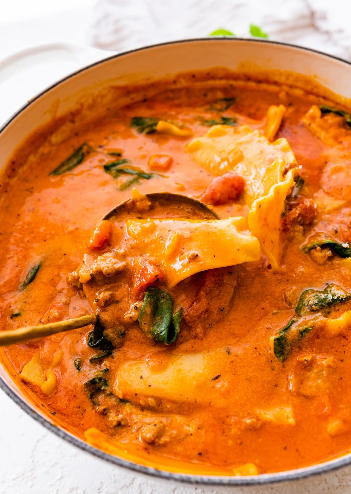 A large pot of lasagna soup with a ladle inside the pot.