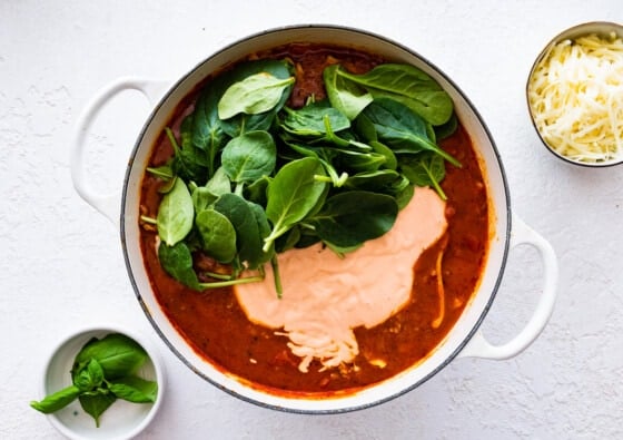 A handful of fresh spinach sits on top of lasagna soup in a large pot.