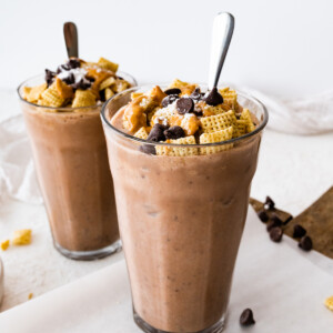 Two muddy buddy protein shakes in large glass cups with a spoon.