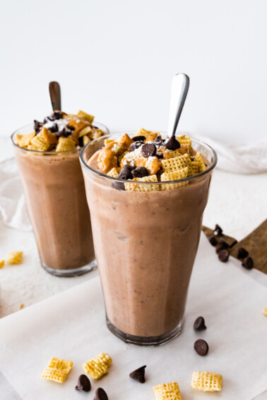 Two muddy buddy protein shakes in large glass cups with a spoon.