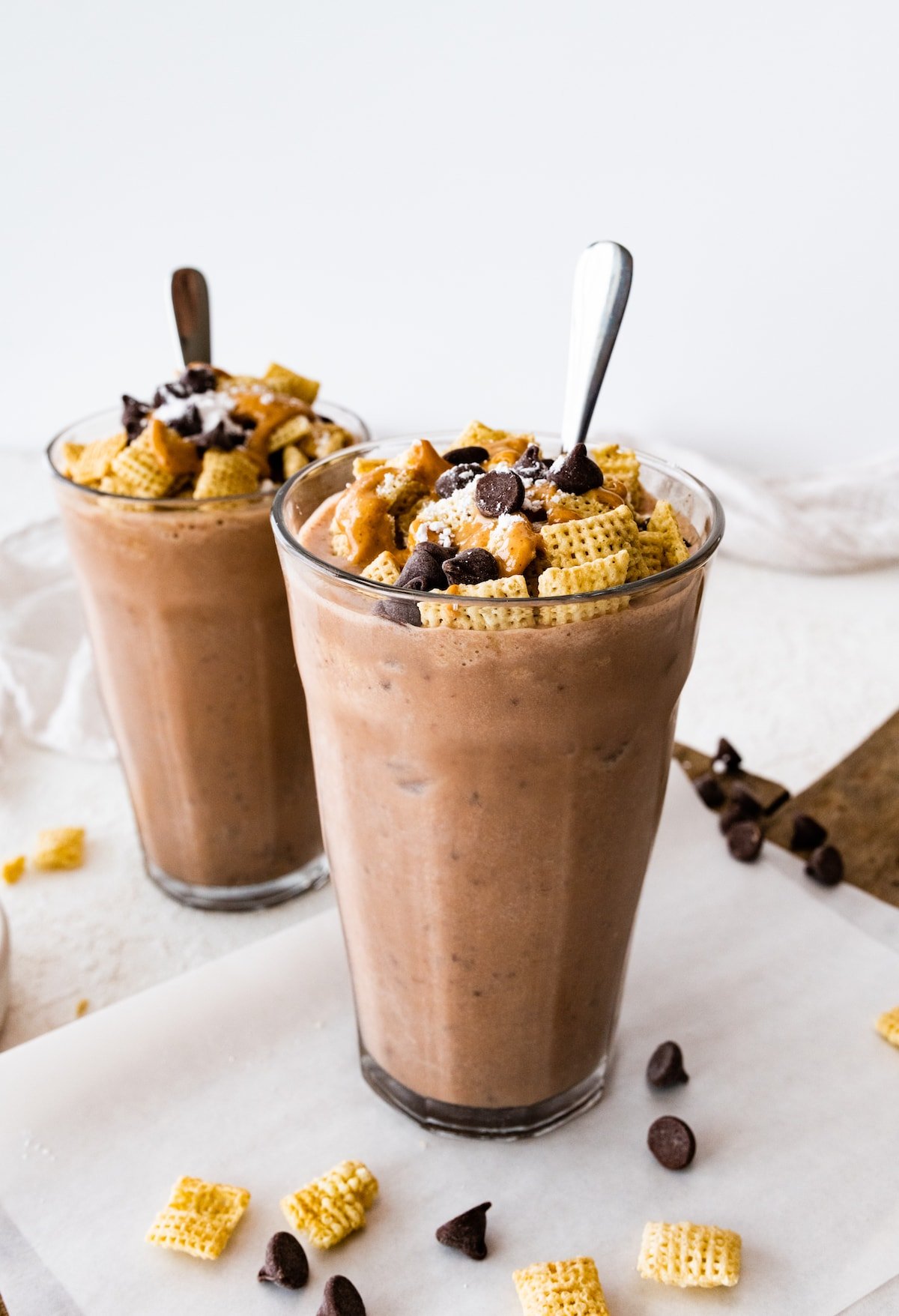 Two muddy buddy protein shakes in large glass cups with a spoon.