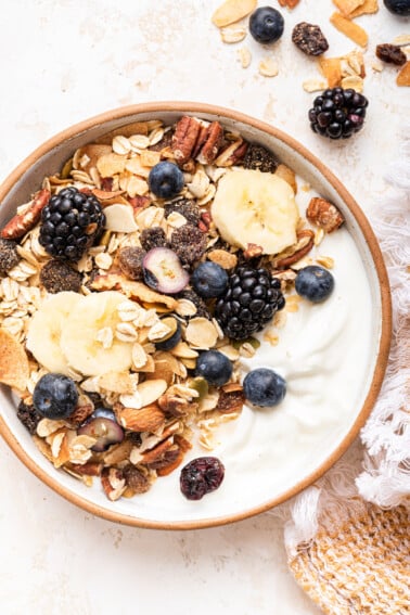 A bowl of yogurt topped with fresh berries, banana slices, and muesli.