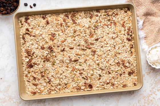 Rolled oats, nuts, and seeds spread out on a baking tray.