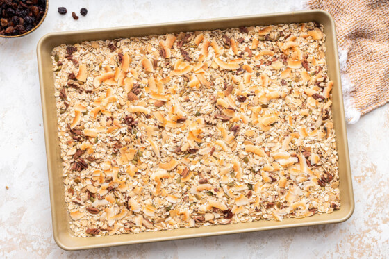 Toasted rolled oats, nuts, and seeds spread out on a baking tray.