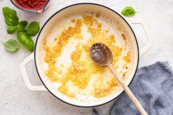 Sauteed onion and garlic in a large pot with a wooden spoon.