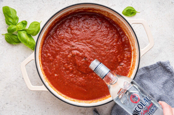 Vodka being poured into the marinara sauce in a large pot.