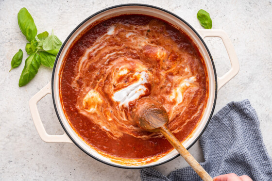 marinara sauce, vodka, and cream being stirred with a wooden spoon in a large pot.