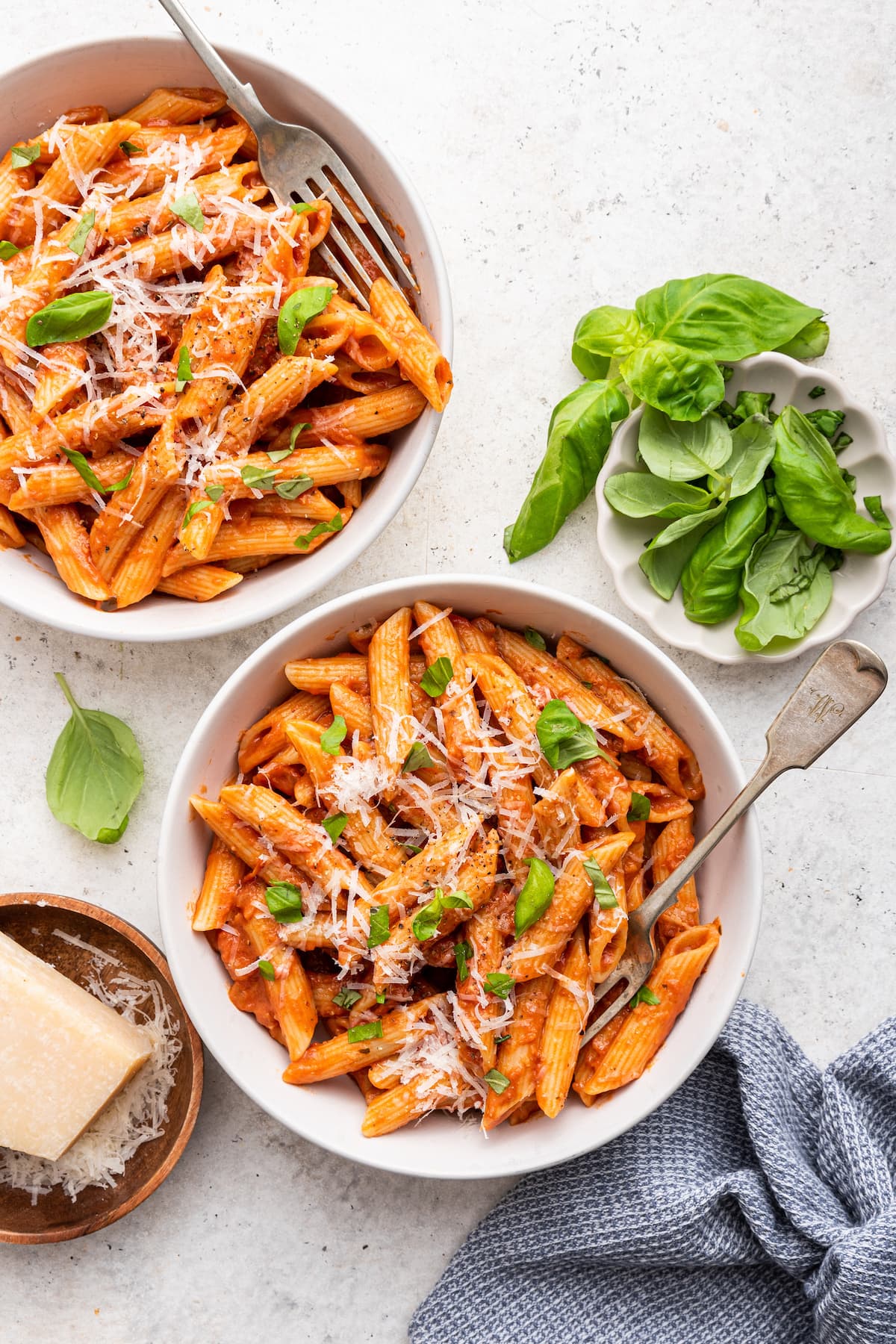 Penne all vodka in two white bowls garnished with fresh basil and a dairy-free parmesan.