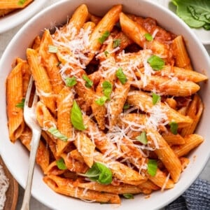 Penne all vodka in a white bowl garnished with fresh basil and a dairy-free parmesan.