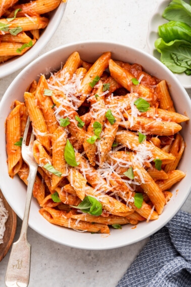 Penne all vodka in a white bowl garnished with fresh basil and a dairy-free parmesan.