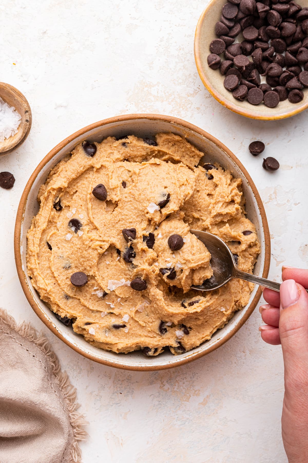 Protein cookie dough in a bowl with a woman's hand using a spoon to take a portion.