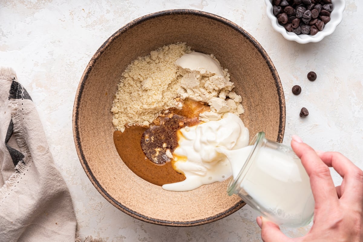 Milk being poured into a mixing bowl of ingredients to be used for a protein cookie dough.
