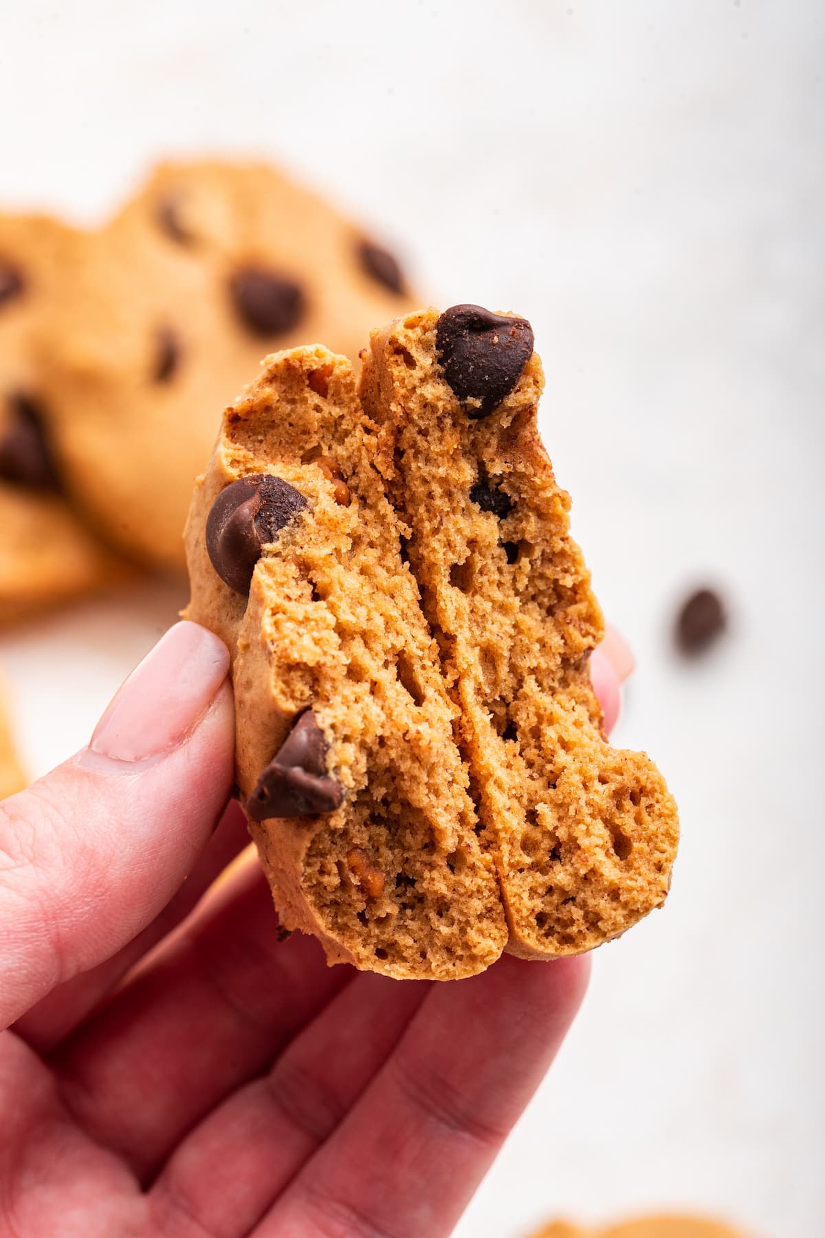 A protein chocolate chip cookie being held in a hand and split in half.