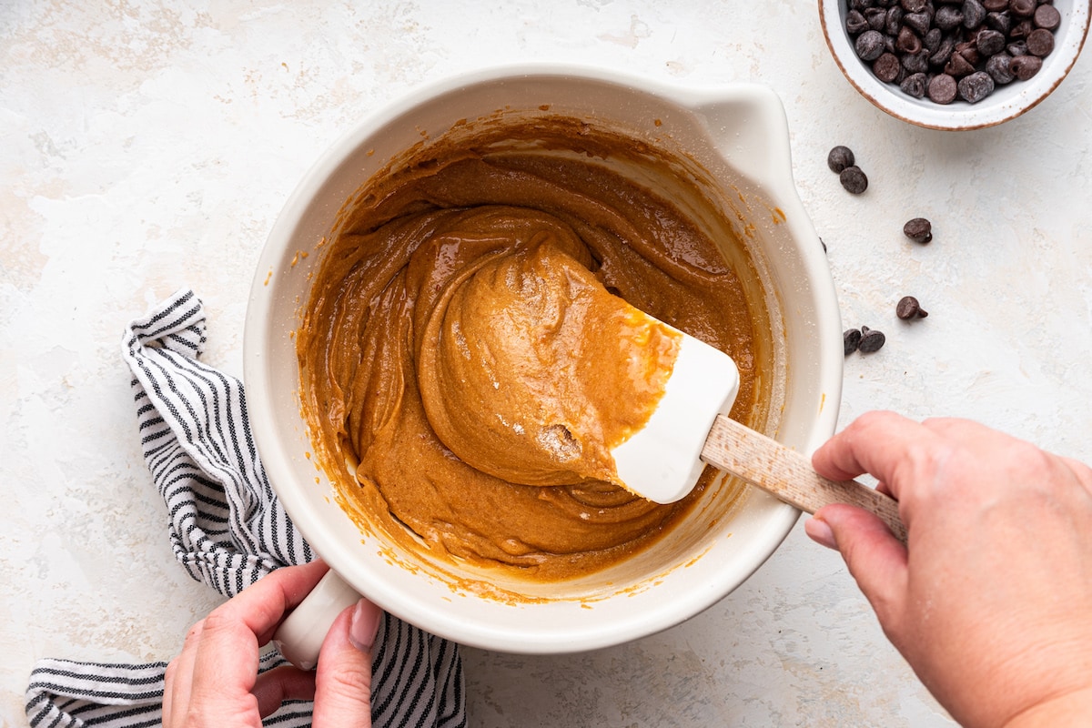 A woman's hand uses a silicone spatula to combine the ingredients to make a dough for the protein cookies.