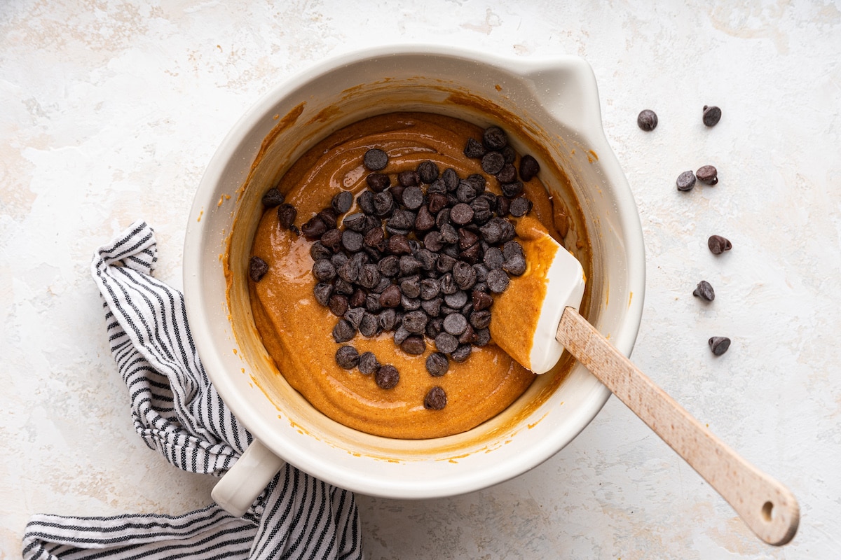 Chocolate chips being added to a large bowl of dough for protein cookies.