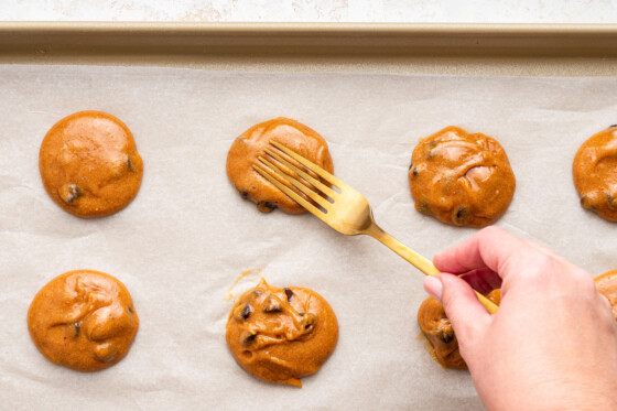 A womans hand using a fork to press each cookie on a baking tray for protein cookies.