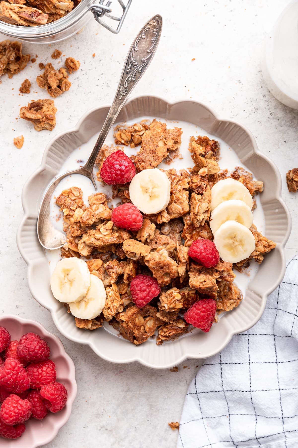 Protein granola in a small bowl with milk, fresh raspberries, and banana slices.