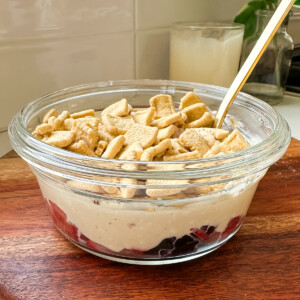 A glass bowl with berries, peanut butter yogurt and Catalina Crunch cereal on top.