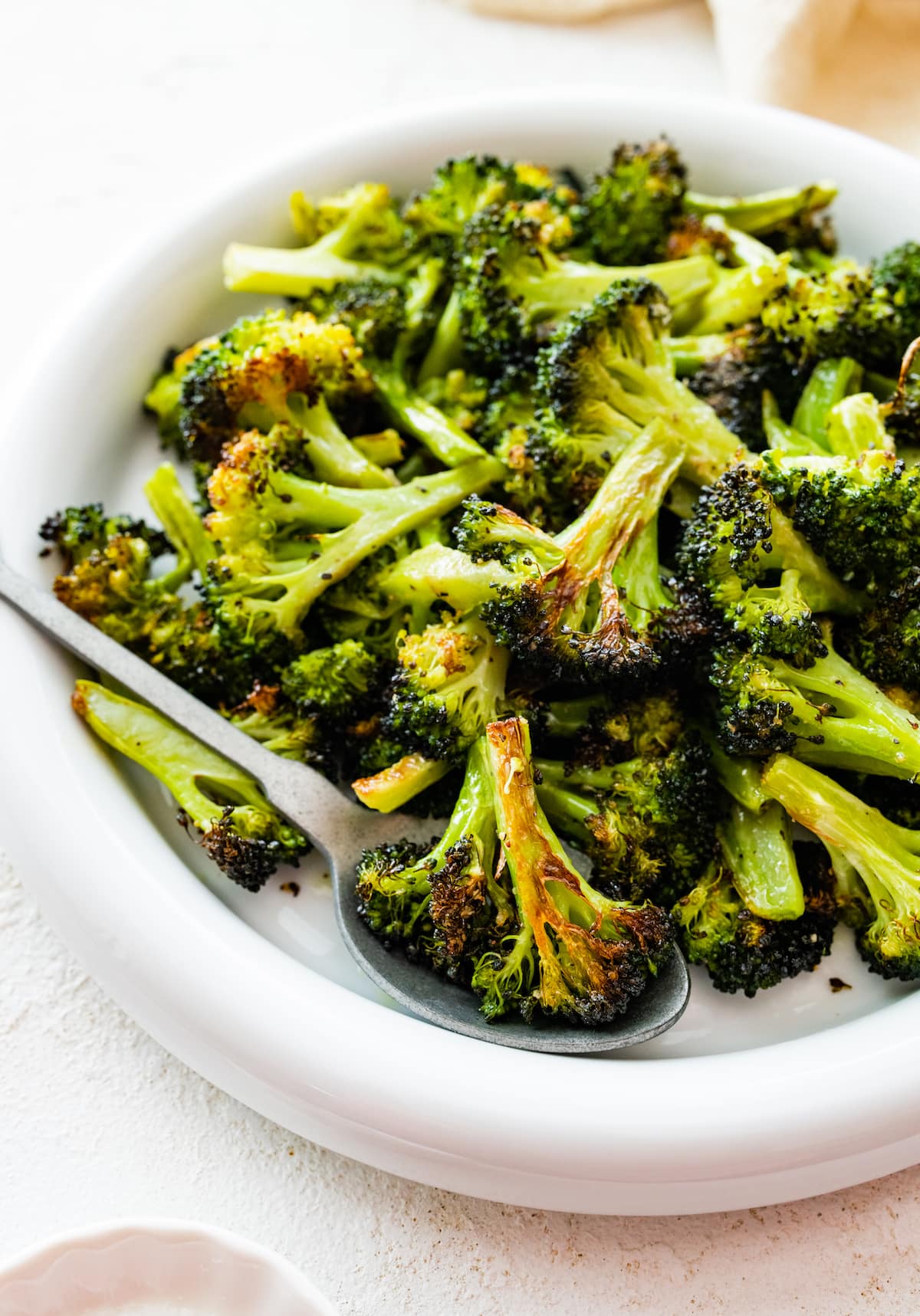 Roasted broccoli on a white plate with a serving spoon.