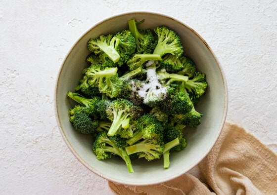 Raw broccoli florets in a mixing bowl with oil and seasoning.
