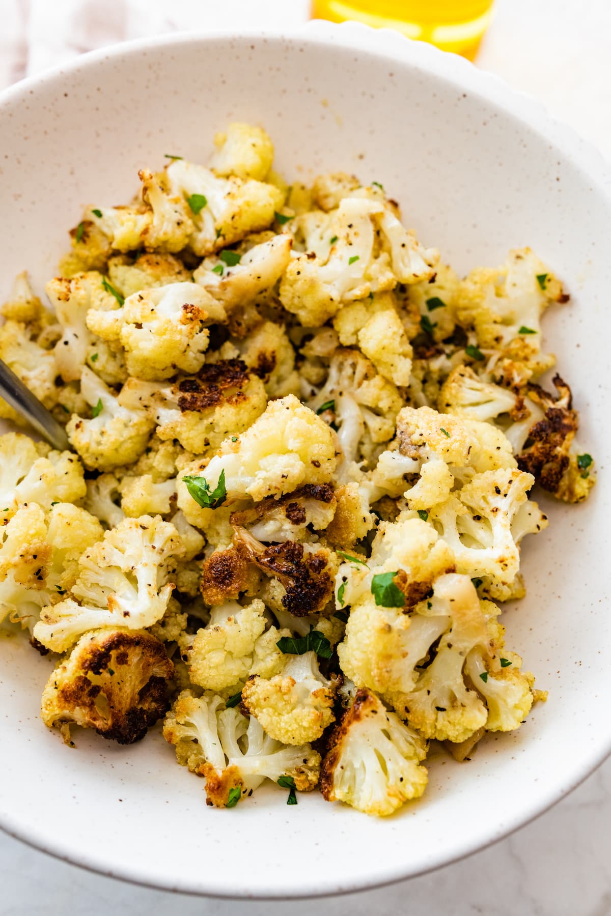 A close up image of roasted cauliflower on a white plate topped with fresh parsley.