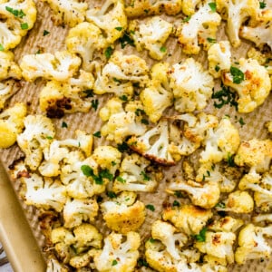 Roasted cauliflower on a baking sheet topped with fresh parsley.