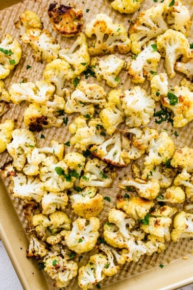 Roasted cauliflower on a baking sheet topped with fresh parsley.