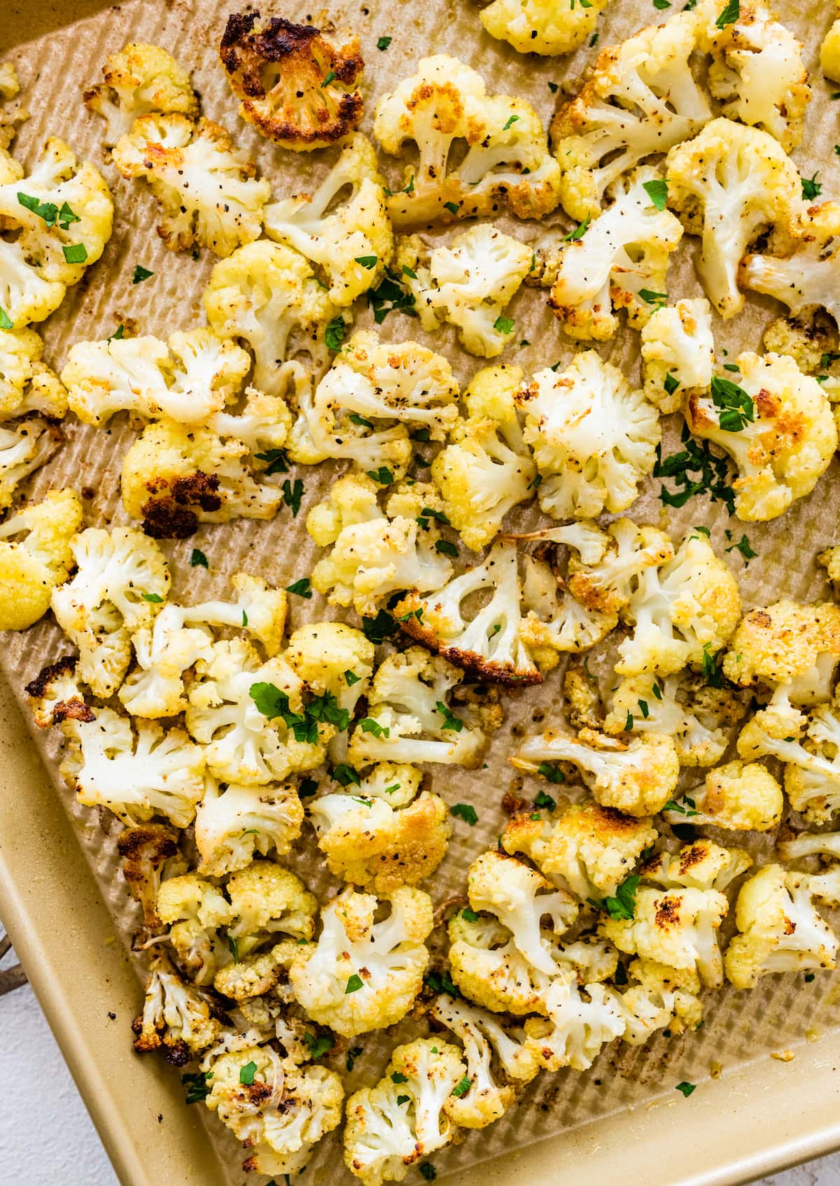 Roasted cauliflower on a baking sheet topped with fresh parsley.