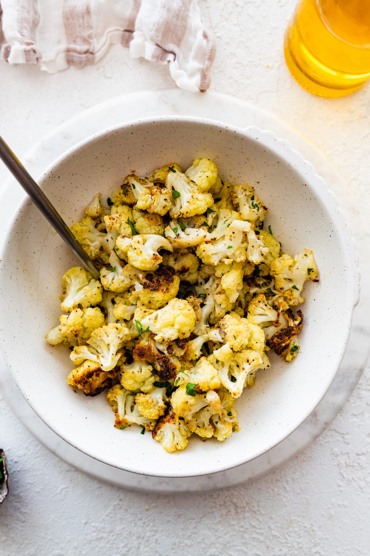 Roasted cauliflower in a white bowl with a metal serving spoon.