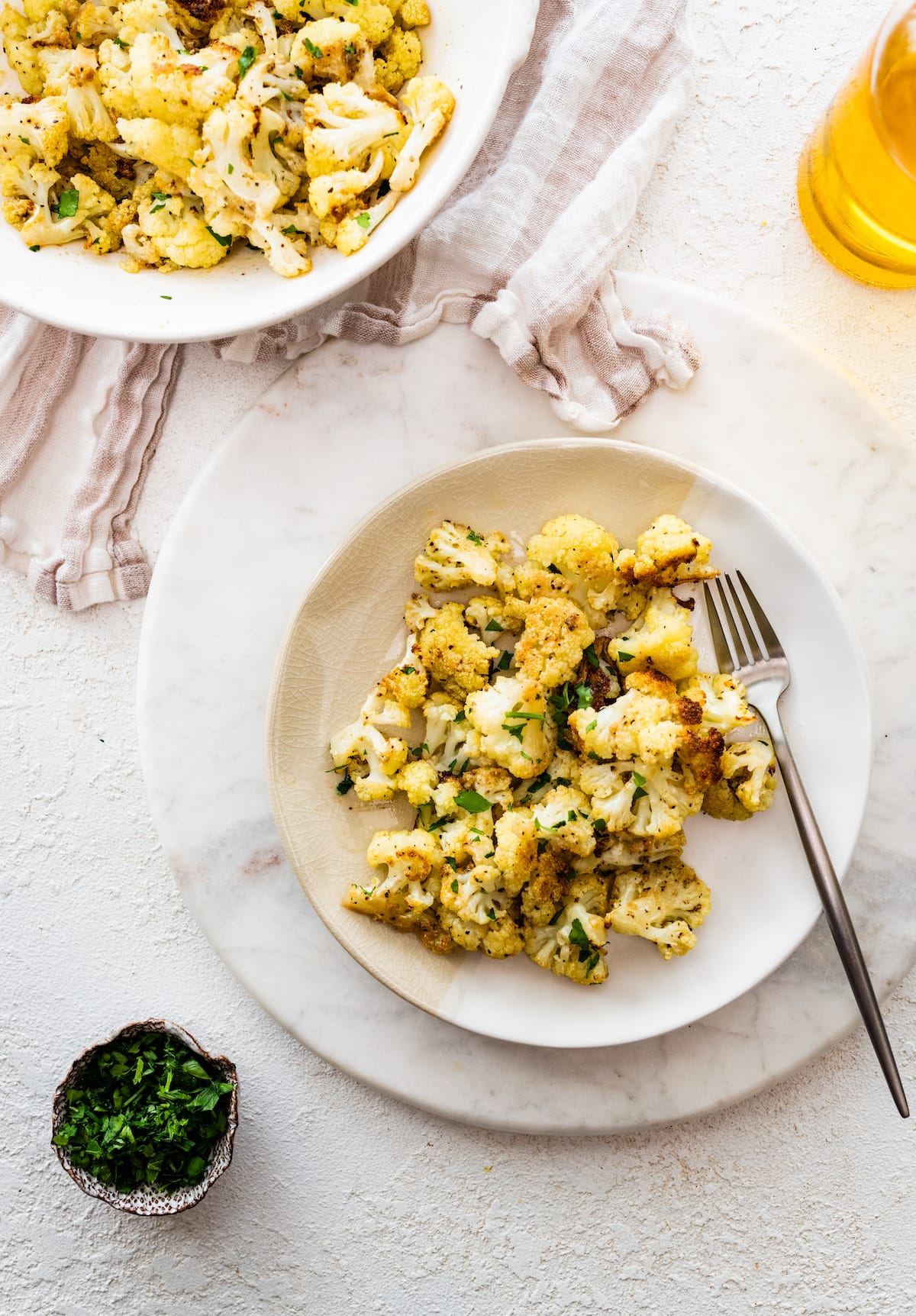 A plate of roasted cauliflower topped with fresh parsley served with a fork.