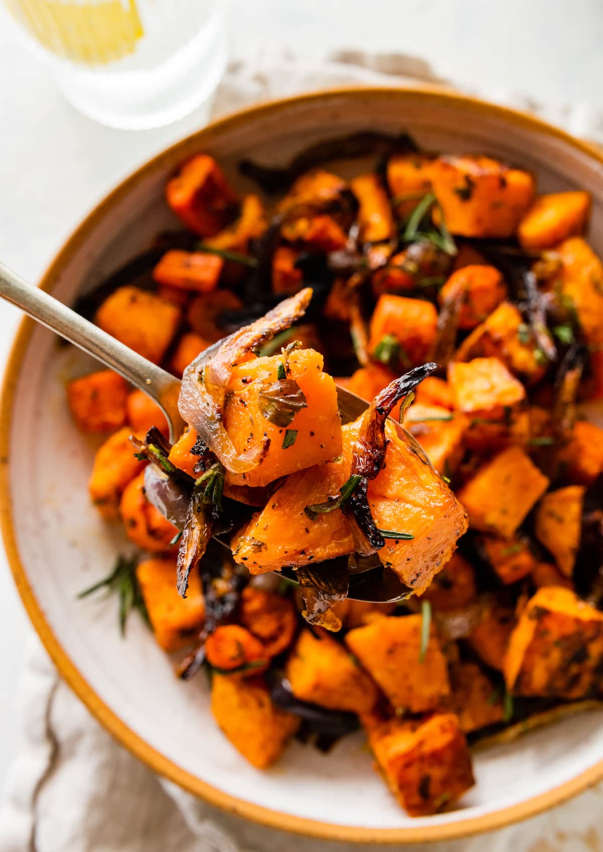 Roasted root vegetables in a bowl with a. spoon holding a bite size portion above this bowl.