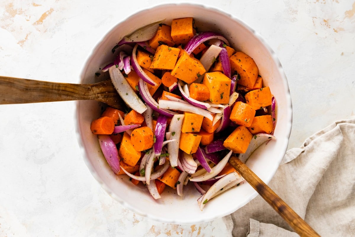 Two wooden serving spoons in a large mixing bowl with root vegetables.
