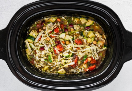 All ingredients for minestrone soup including beans, vegetables, herbs, and spices in a large crock pot.