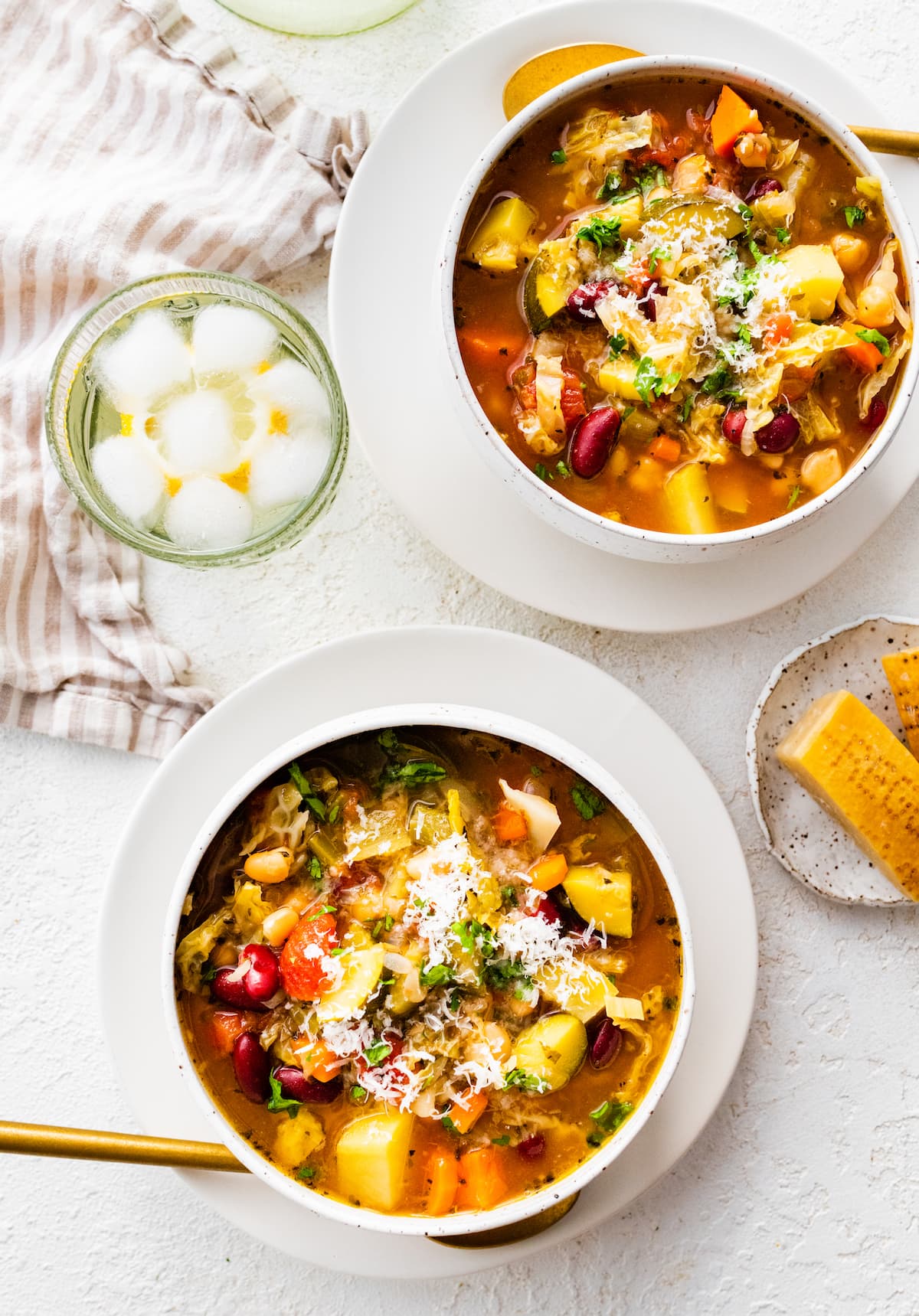 Two bowls of minestrone soup on plates.