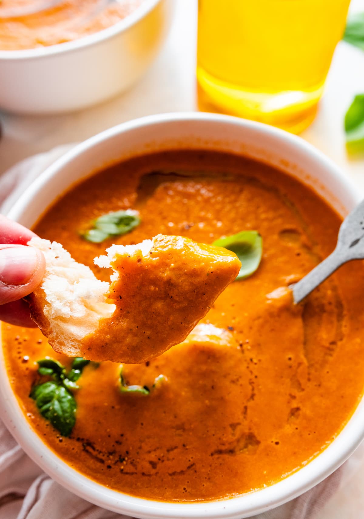 A womans hand holding a piece of bread that has been dipped in a bowl of tomato basil soup.