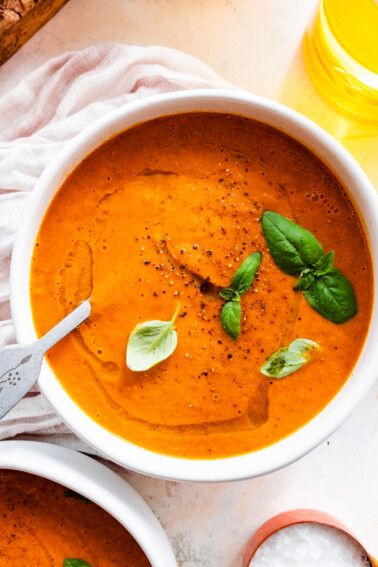 Tomato basil soup garnished with a drizzle of oil and fresh basil in a bowl.