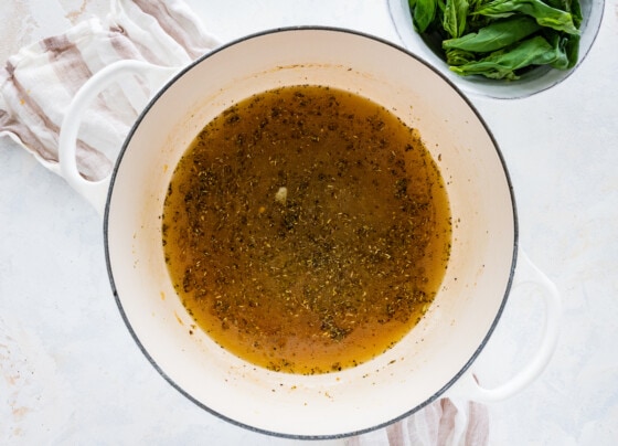 Broth added to a large pot of onions, herbs, and spices.