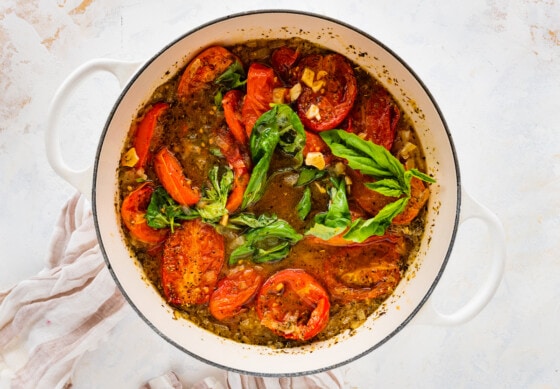 A large pot with fresh basil, roasted tomatoes, onions, herbs, spices, and broth.