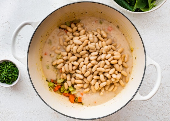 White beans added to a large pot of vegetables.