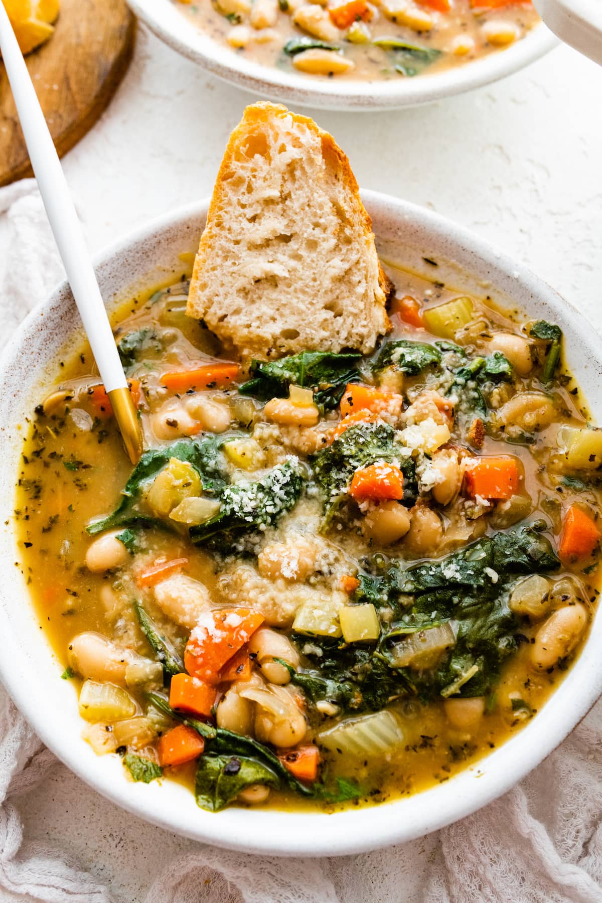 White bean soup in a bowl with a half of a slice of bread in the soup.