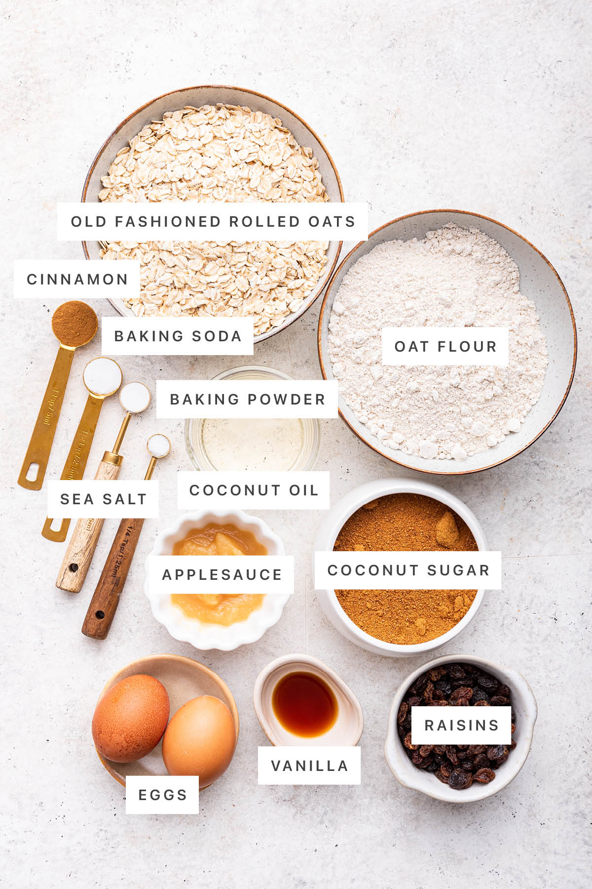 Ingredients measured out to make Oatmeal Raisin Cookies: oats, oat flour, cinnamon, baking soda, baking powder, coconut oil, sea salt, applesauce, coconut sugar, eggs, vanilla and raisins.