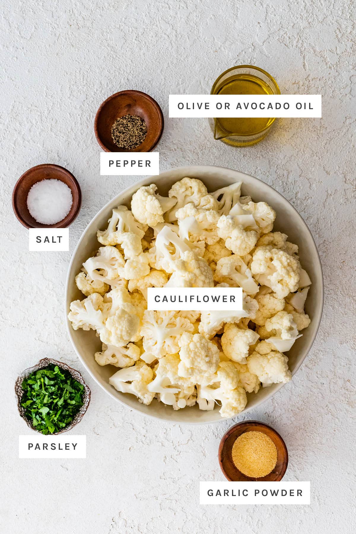 Ingredients measured out to make roasted cauliflower: cauliflower, olive/avocado oil, garlic powder, salt, pepper and parsley.