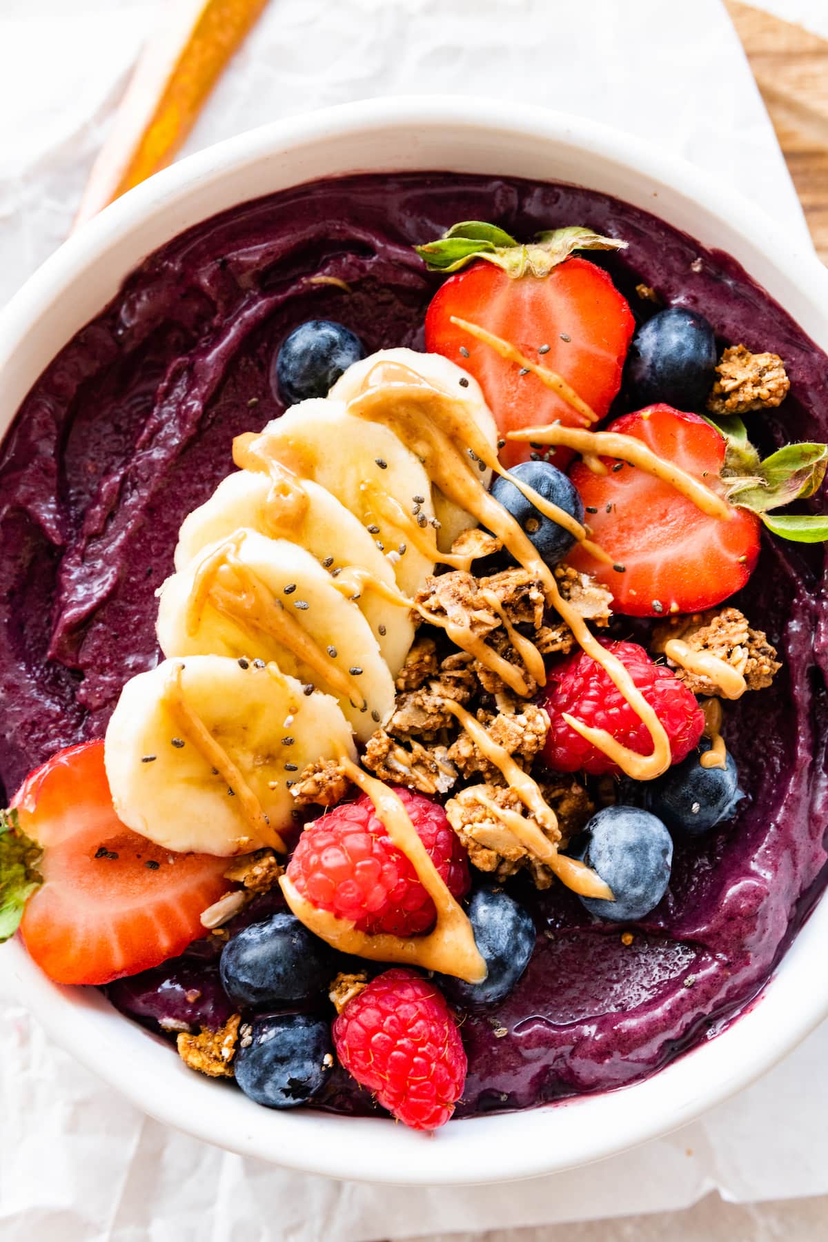 An acai bowl topped with fresh berries, sliced banana, granola, and a drizzle of nut butter.